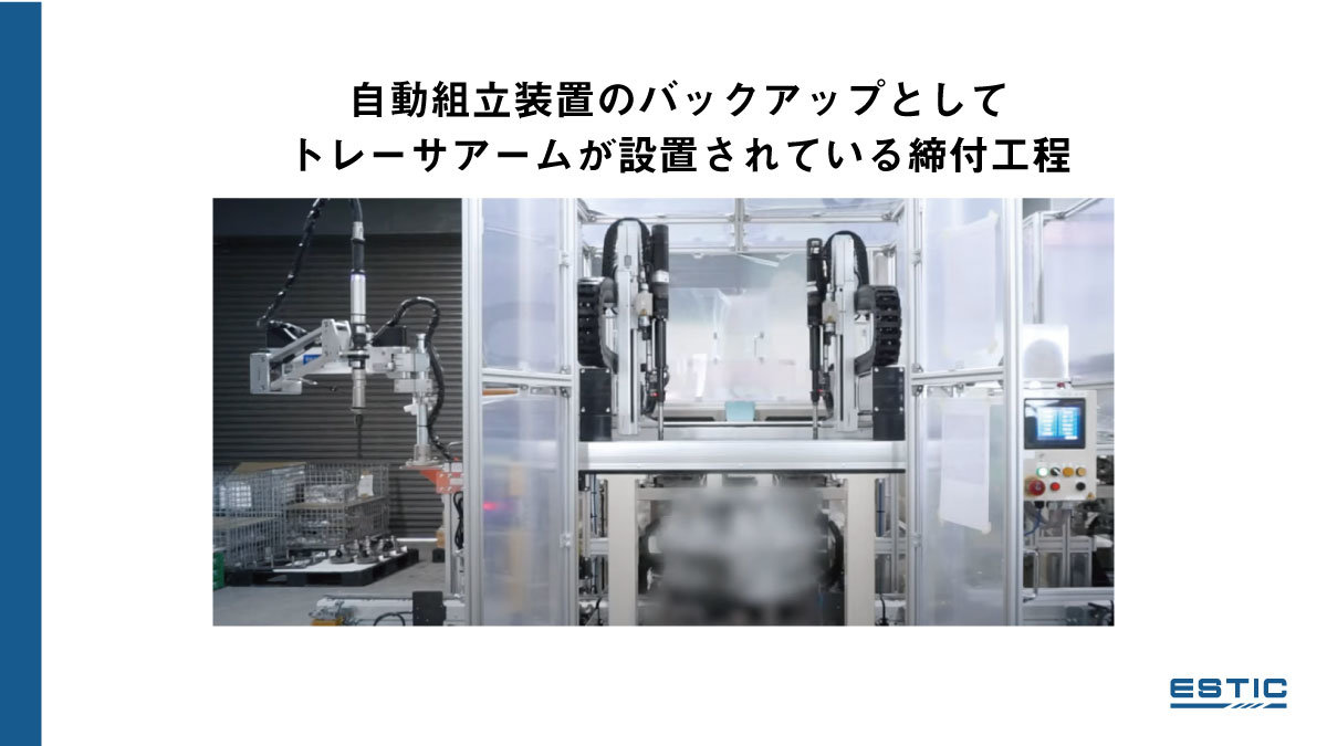 自動組立装置のバックアップとしてトレーサアームが設置されている締付工程の実際の写真。直交ロボットが２台ついた自動組立装置の左脇にトレーサアームが設置されている。